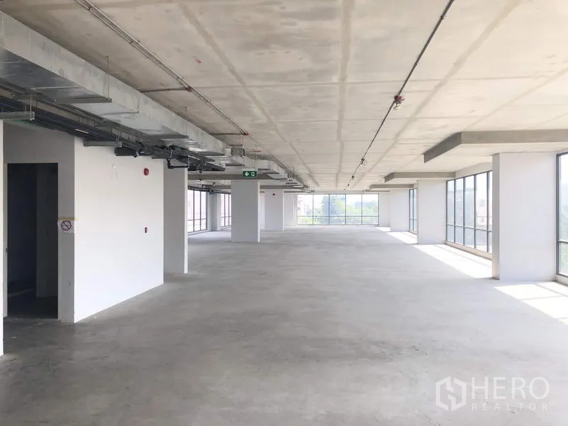 办公空间 出租在Suan Luang, Bangkok - 明亮通透的开放办公区，多根立柱与大面积玻璃，并设有紧急出口指示。