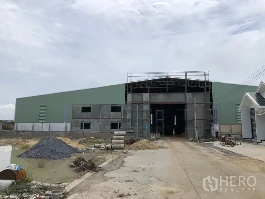 Warehouse for rent or sale in Sai Noi, Nonthaburi - Front exterior of a large steel-frame warehouse under construction with a wide entry and driveway.