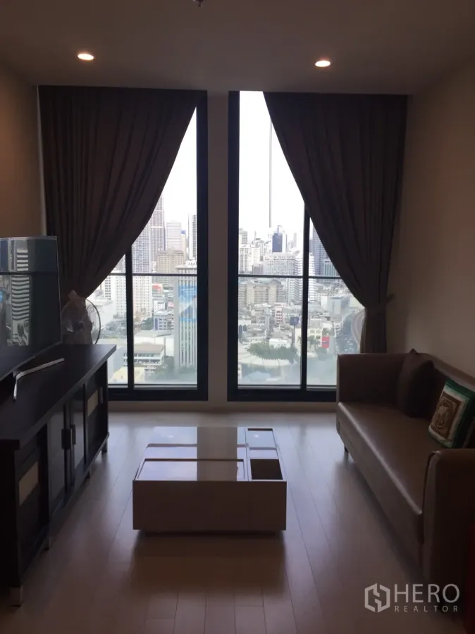 คอนโด ให้เช่าในPathum Wan, Bangkok - ห้องนั่งเล่นมีหน้าต่างสูงจรดเพดาน วิวสกายไลน์กรุงเทพ พร้อมโซฟาและโต๊ะกลาง