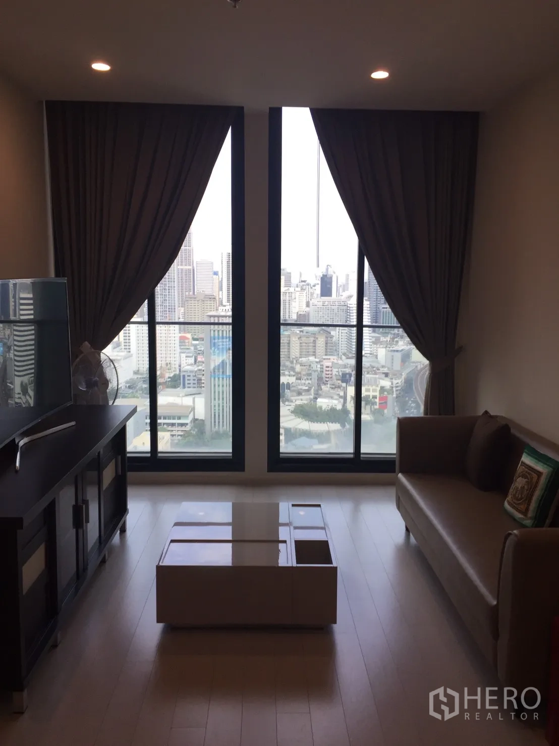 คอนโด ให้เช่าในPathum Wan, Bangkok - ห้องนั่งเล่นมีหน้าต่างสูงจรดเพดาน วิวสกายไลน์กรุงเทพ พร้อมโซฟาและโต๊ะกลาง