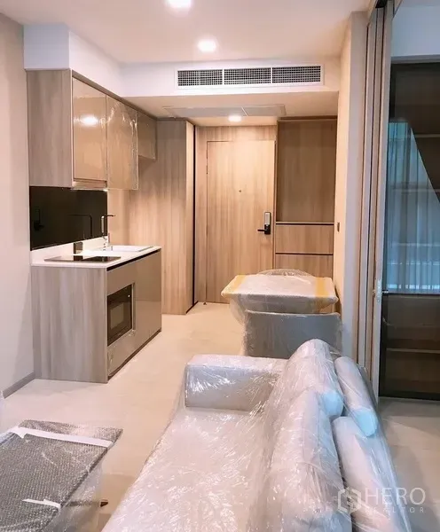 公寓 出租在Watthana, Bangkok - 开放式起居区，配内置小厨房、木质柜体和全新包膜家具。