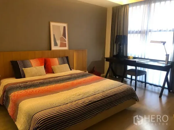 Condominium for rent in Watthana, Bangkok - Bright bedroom with king bed, wood headboard, and a work desk by a large window with sheer curtains.
