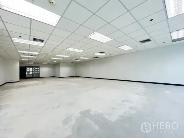 Office Space for rent in Khlong Toei, Bangkok - Spacious open-plan office with grid ceiling, LED lighting, AC vents, white walls and a rear glass entry.