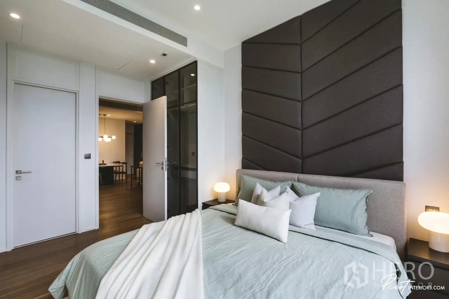 Condominium for rent in Pathum Wan, Bangkok - Cozy bedroom featuring a padded headboard wall, bedside lamps, and doorway to the living area.