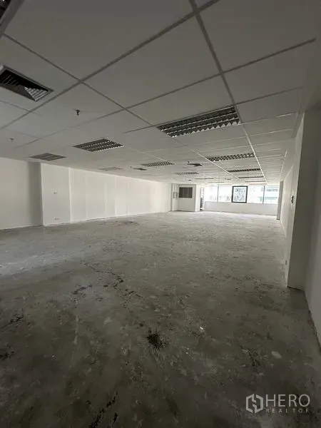 办公空间 出租在Pathum Wan, Bangkok - 开放式办公室内景，方格吊顶、荧光灯、裸露混凝土地面与大窗。