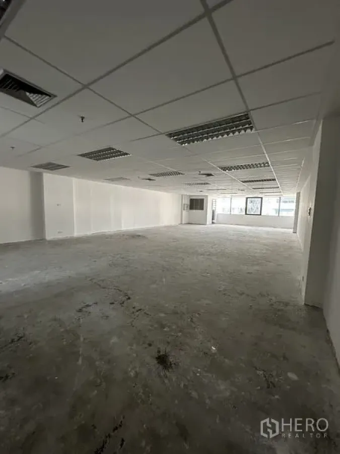 办公空间 出租在Pathum Wan, Bangkok - 开放式办公室内景，方格吊顶、荧光灯、裸露混凝土地面与大窗。