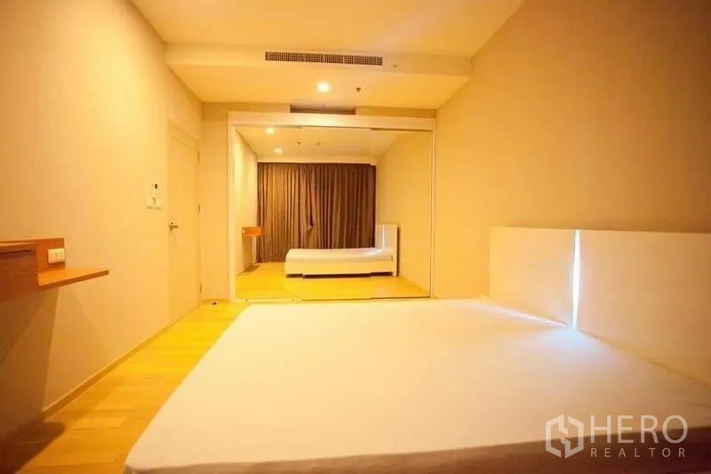 Condominium for rent or sale in Watthana, Bangkok - Spacious bedroom with wood floors, mirrored wardrobe wall and soft lighting.