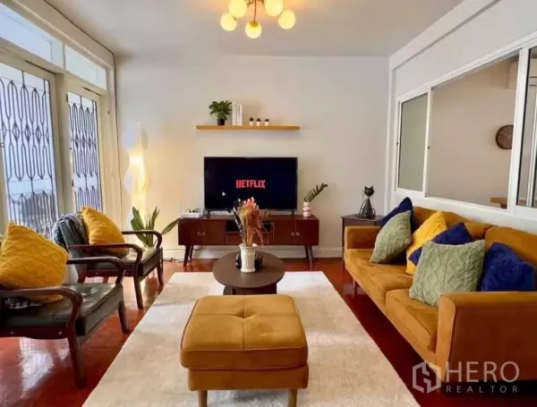 Townhouse for rent in Watthana, Bangkok - Cozy living room with mustard sofa, TV console, modern lighting and balcony doors.