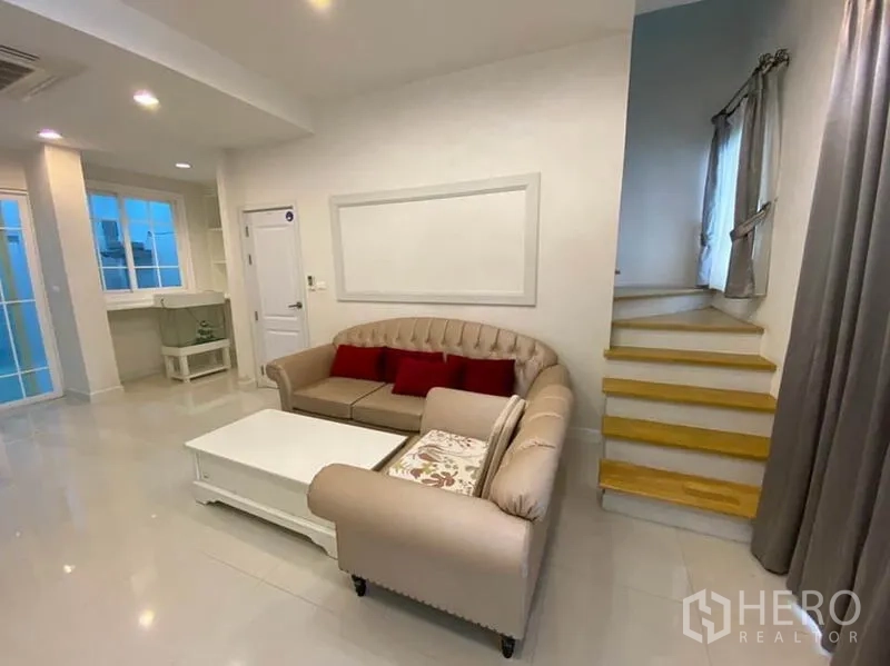 ทาวน์เฮาส์ ให้เช่าในBang Na, Bangkok - ห้องนั่งเล่นโทนสว่างมีโซฟาชุด โต๊ะกลาง ไฟดาวน์ไลท์ และบันได