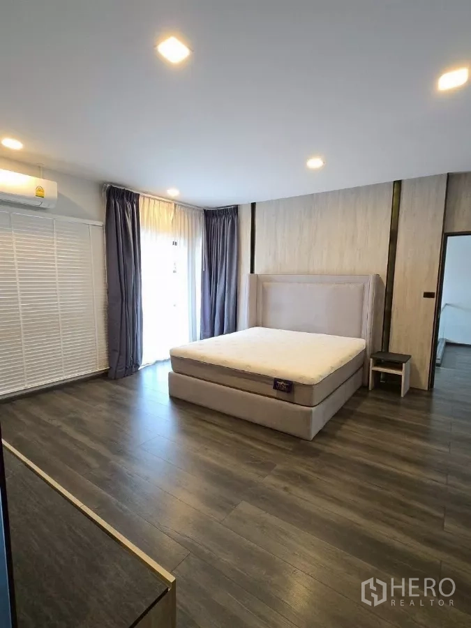 Townhouse for rent in Bang Phli, Samut Prakan - Large master bedroom with upholstered bed, wood flooring, and wide windows with blackout and sheer curtains.