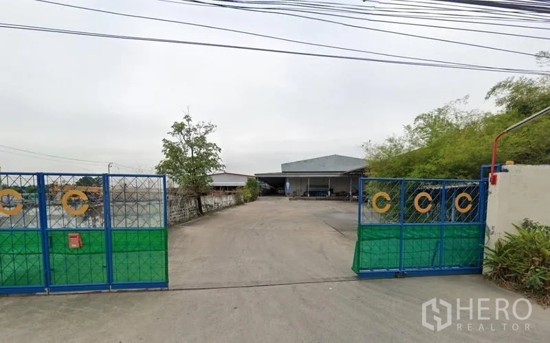 货栈 出租在Bang Phli, Samut Prakan - 带蓝色大门的仓库入口，宽阔混凝土车道，后方金属屋顶仓库，位于邦普里北榄府。