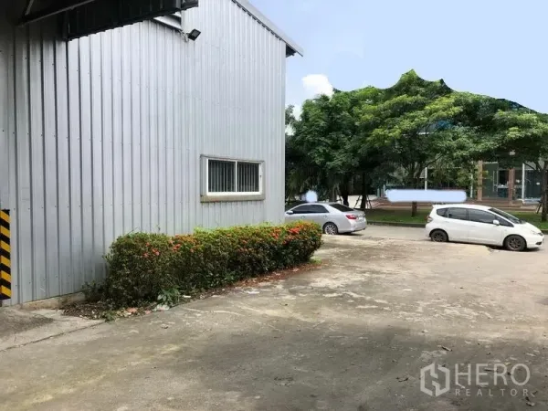 คลังสินค้า ให้เช่าในPak Kret, Nonthaburi - มุมด้านข้างโกดัง มีหน้าต่าง เตียงต้นไม้ และพื้นที่จอดรถกว้างติดถนนร่มรื่น