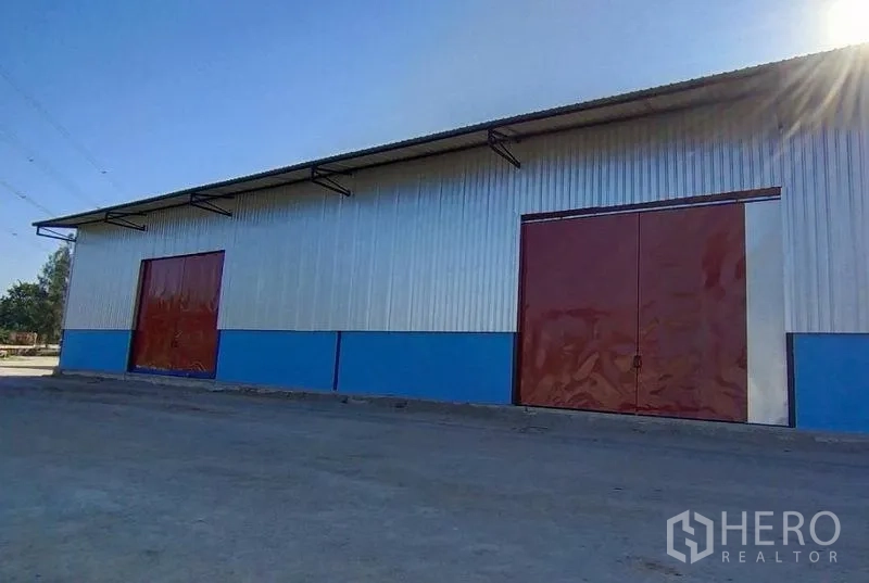 Warehouse for rent in Si Racha, Chon Buri - Angle view of the warehouse facade with multiple steel sliding doors and driveway access.