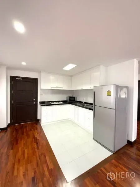 คอนโด ให้เช่าในWatthana, Bangkok - ครัวรูปตัว U สีขาว เคาน์เตอร์หินสีดำ อ่างล้างมือ เตา และตู้เย็นสูง อยู่ติดทางเข้า พื้นกระเบื้อง