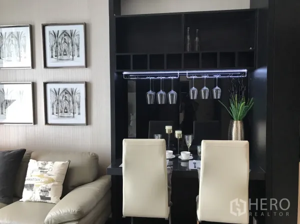 คอนโด ให้เช่าหรือขายในWatthana, Bangkok - มุมรับประทานอาหารพร้อมที่แขวนแก้วไวน์ เก้าอี้สีขาว และภาพตกแต่ง ข้างโซฟาในห้องนั่งเล่นคอนโด