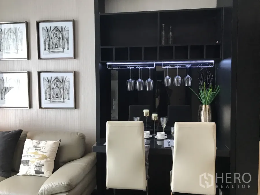 คอนโด ให้เช่าหรือขายในWatthana, Bangkok - มุมรับประทานอาหารพร้อมที่แขวนแก้วไวน์ เก้าอี้สีขาว และภาพตกแต่ง ข้างโซฟาในห้องนั่งเล่นคอนโด