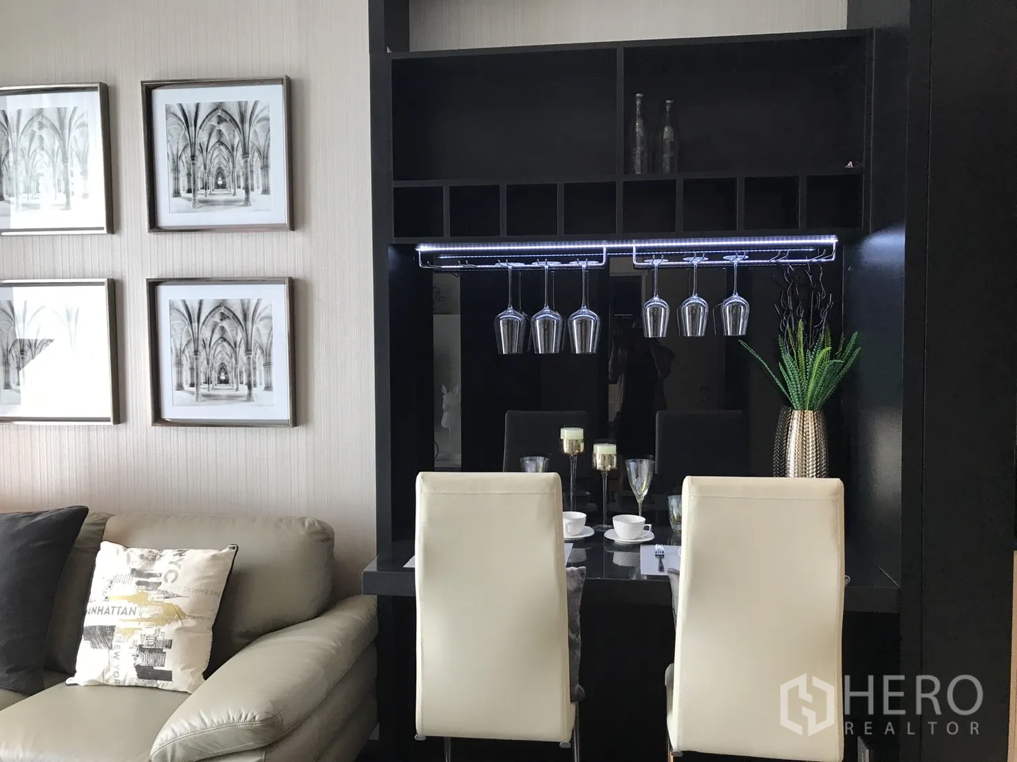 คอนโด ให้เช่าหรือขายในWatthana, Bangkok - มุมรับประทานอาหารพร้อมที่แขวนแก้วไวน์ เก้าอี้สีขาว และภาพตกแต่ง ข้างโซฟาในห้องนั่งเล่นคอนโด