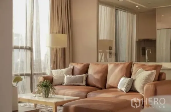 คอนโด ให้เช่าในSathon, Bangkok - โซฟาหนังสีน้ำตาลพร้อมหมอนอิงและโคมไฟยืน โดยมีครัวโมเดิร์นด้านหลัง