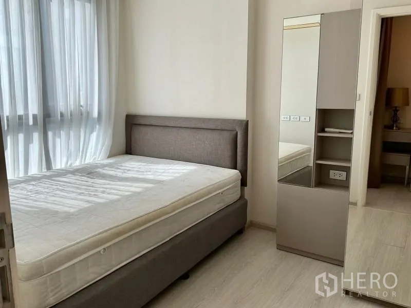 Condominium for sale in Khlong Toei, Bangkok - Bright condo bedroom with upholstered bed, sheer curtains and a mirrored wardrobe.