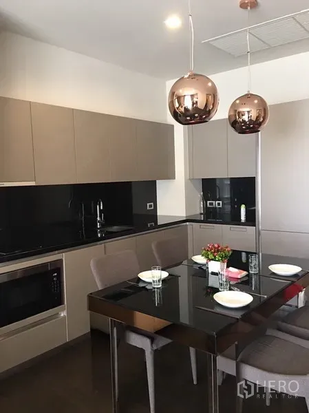 Condominium for rent in Watthana, Bangkok - Dining zone beside sleek kitchen with glossy black countertops and twin copper pendant lights.