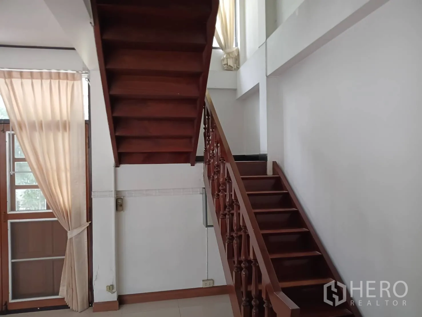 Detached House for sale in Watthana, Bangkok - Wooden staircase with handrail beside a tall window and curtains.
