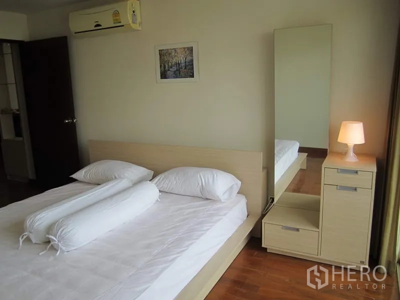 คอนโด ให้เช่าในBang Rak, Bangkok - ห้องนอนแขกปูผ้าปูสีขาว โต๊ะข้างพร้อมโคมไฟ กระจกตัวเต็ม และเครื่องปรับอากาศ