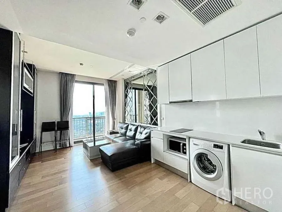 Condominium for rent in Bangkok - Another angle of the living room showing sleek white kitchen and balcony access.