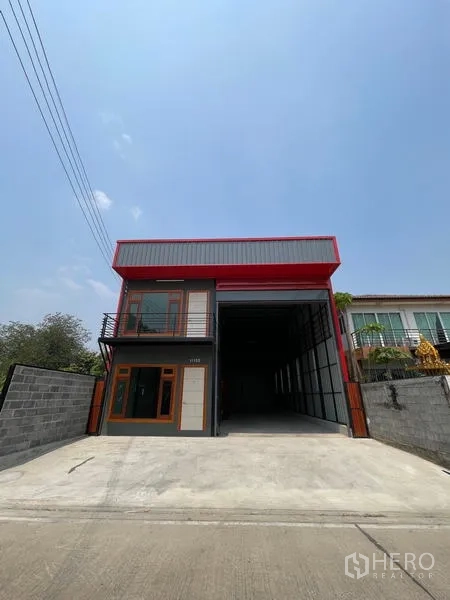 货栈 出租在Lam Luk Ka, Pathum Thani - 街景正面：红色檐口的现代高仓仓库，宽阔混凝土车道与围墙大门。