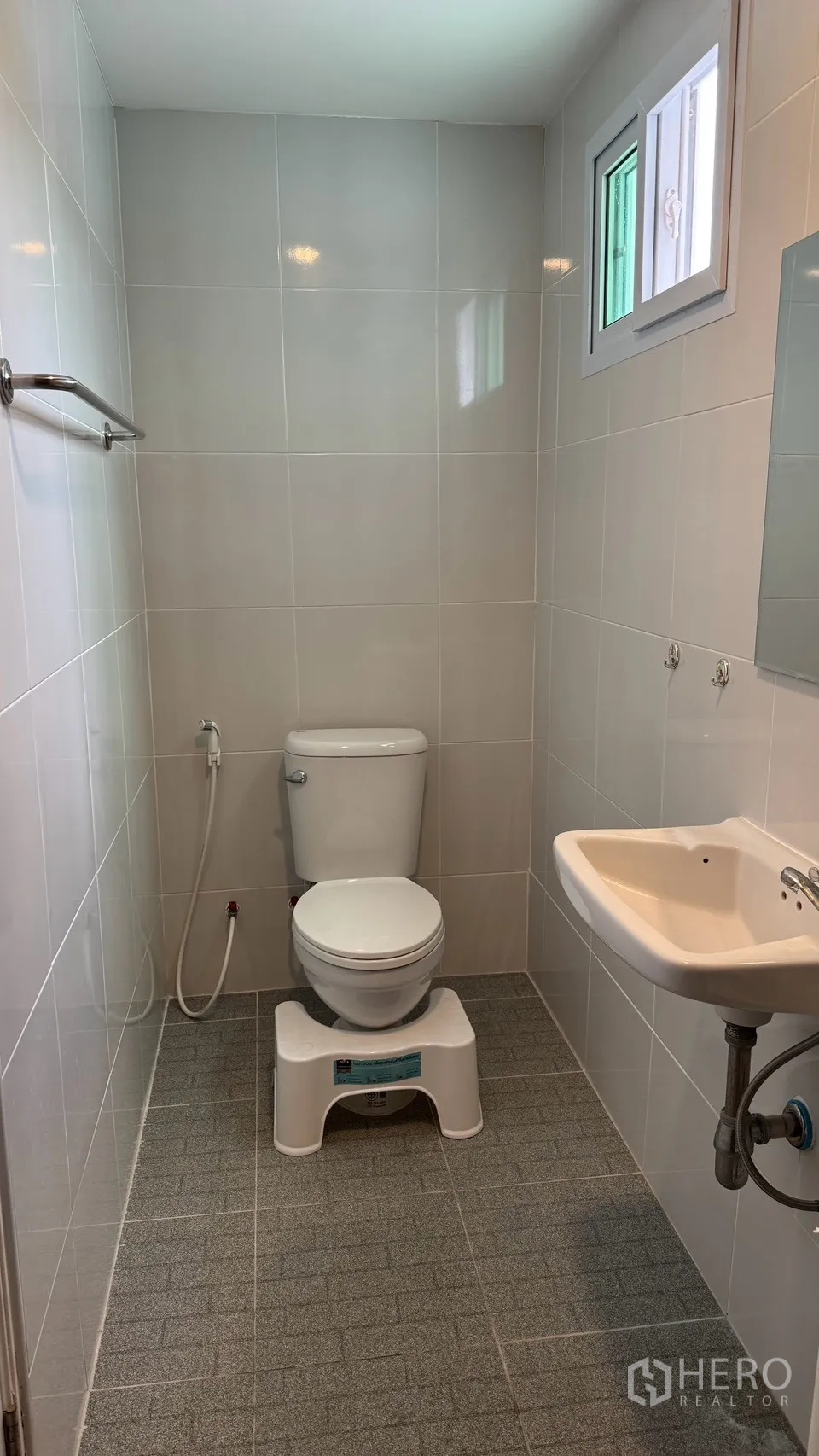Detached House for rent in Saphan Sung, Bangkok - Minimal bathroom with light tiles, toilet, bidet spray, small sink, and window.