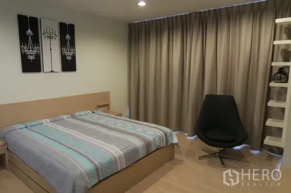 Condominium for rent in Huai Khwang, Bangkok - Master bedroom with king bed, wall art, swivel chair and built‑in shelving with floor‑to‑ceiling drapes.