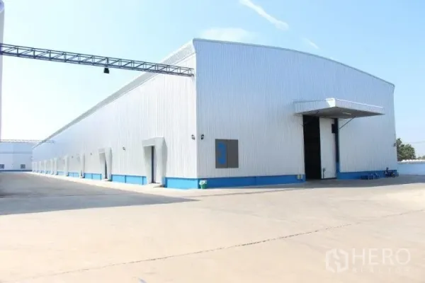 Warehouse for rent in Pathum Thani - Long warehouse building with multiple bay doors along a wide concrete service road.