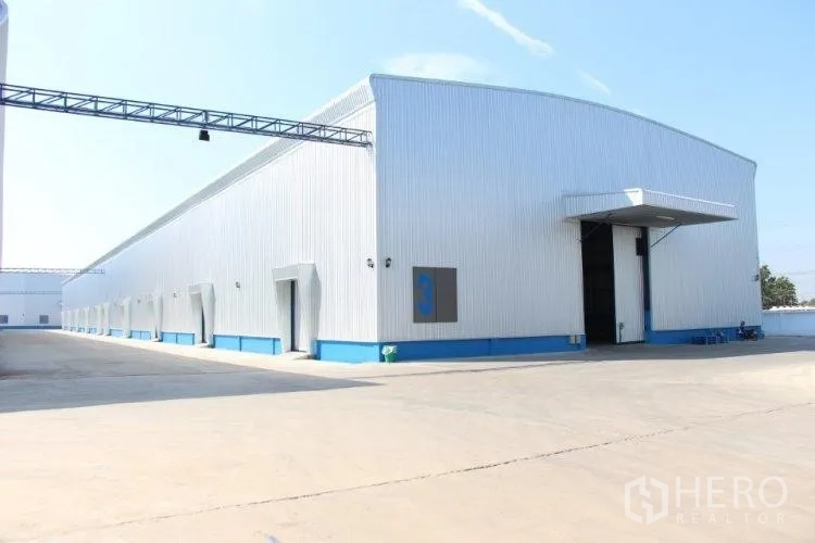 Warehouse for rent in Pathum Thani - Long warehouse building with multiple bay doors along a wide concrete service road.