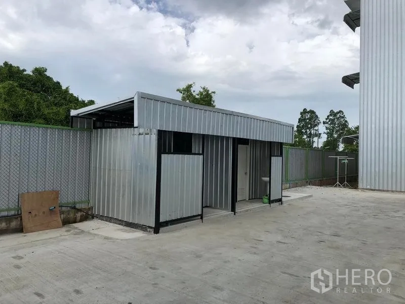 Warehouse for rent in Pathum Thani - Detached utility block with corrugated metal walls housing restrooms on a paved yard beside the warehouse.