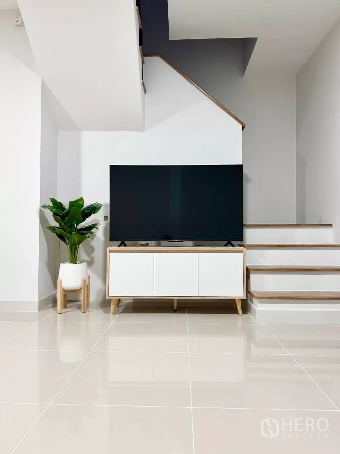 Townhouse for rent in Bang Phli, Samut Prakan - Minimalist living area with large flat-screen TV on console and staircase nearby.