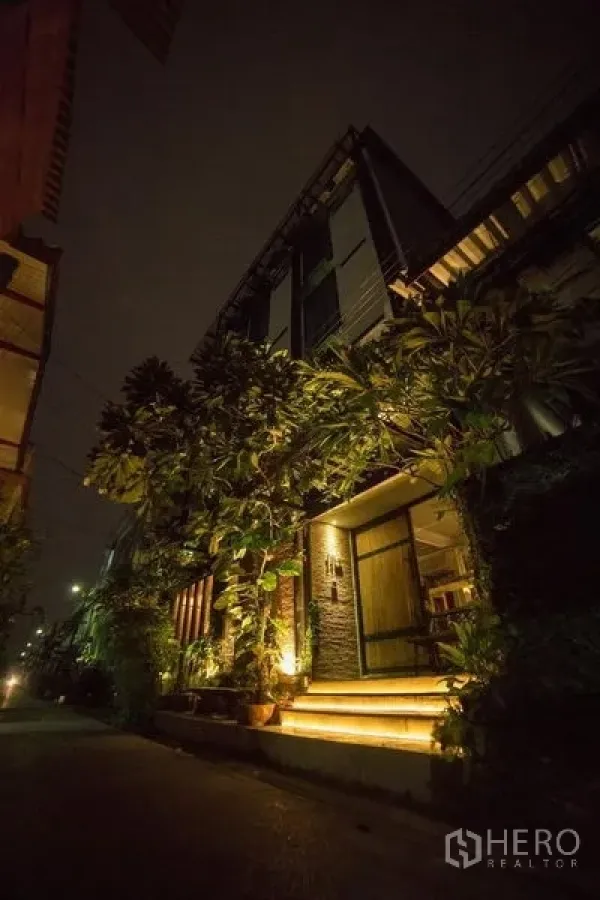 店屋 出租或出售在Din Daeng, Bangkok - 夜间外观，多层临街商铺楼，外墙暖色灯光、绿植和通往入口的台阶。