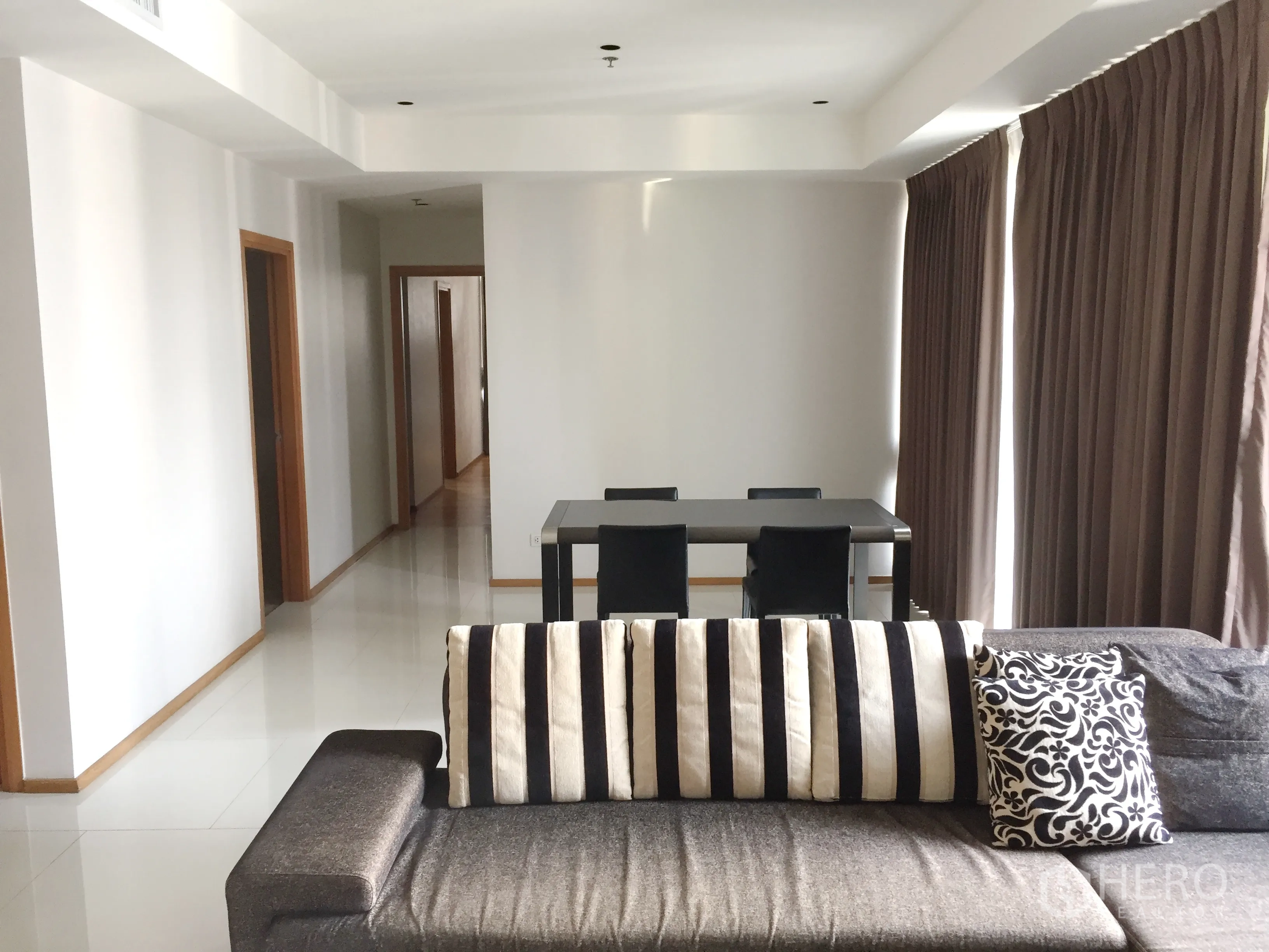 คอนโด ให้เช่าในKhlong Toei, Bangkok - พื้นที่นั่งเล่นกว้างพร้อมโซฟาหมอนลายทาง ชุดโต๊ะอาหาร 4 ที่นั่ง และโถงทางเดินไปยังห้องนอน