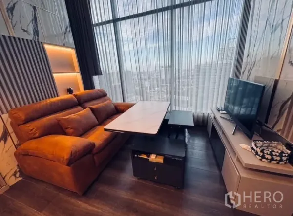 Condominium for rent in Chatuchak, Bangkok - Living room with adjustable marble coffee table, TV console, and skyline behind sheer curtains.