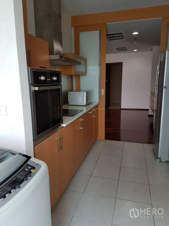 Condominium for rent or sale in Watthana, Bangkok - Galley kitchen with built-in oven, range hood, wood cabinetry, and washing machine.