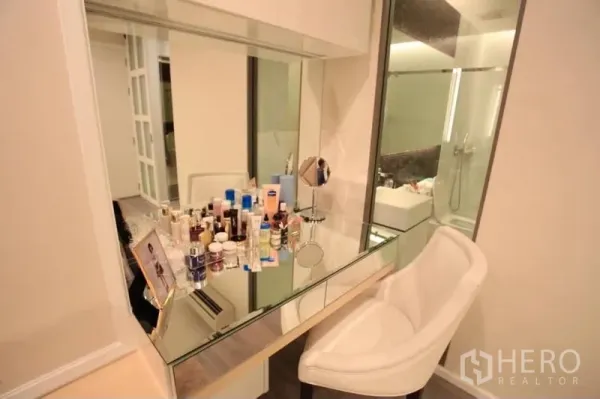 Condominium for rent or sale in Watthana, Bangkok - Built-in vanity with large mirror and chair beside a glass-walled bathroom.