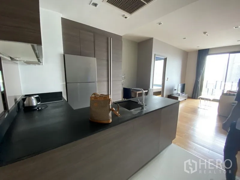 Condominium for rent in Khlong Toei, Bangkok - Modern open-plan kitchen with dark stone countertop, island sink and built-in cabinetry facing the living area