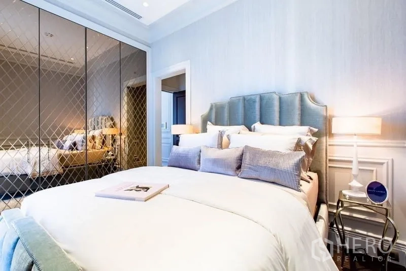 Condominium for sale in Pathum Wan, Bangkok - Stylish bedroom with tufted blue headboard and mirrored wardrobe with lattice pattern.