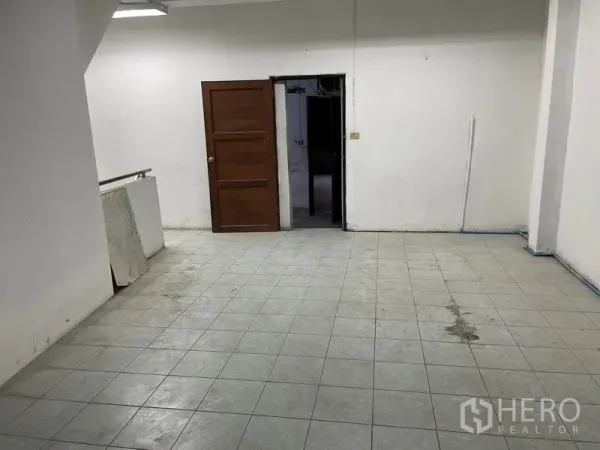 Shophouse for rent in Watthana, Bangkok - Back room with gray tiled floor and a wooden door, ideal for storage or staff use.