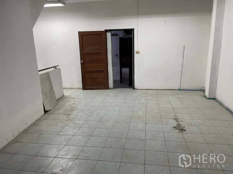 Shophouse for rent in Watthana, Bangkok - Back room with gray tiled floor and a wooden door, ideal for storage or staff use.