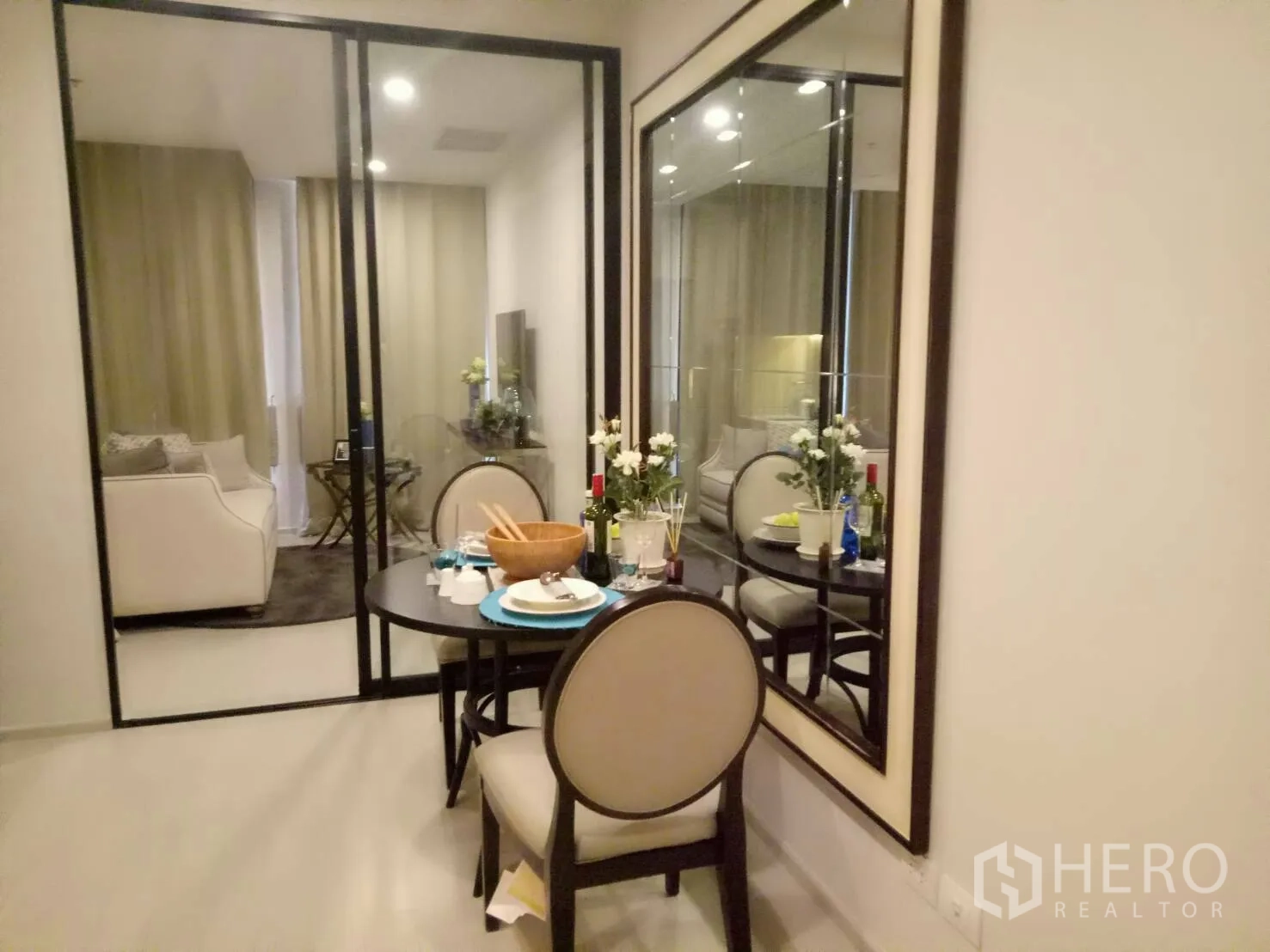 Condominium for rent or sale in Pathum Wan, Bangkok - Compact dining area set for two beside a large wall mirror and sliding glass doors to the living area.