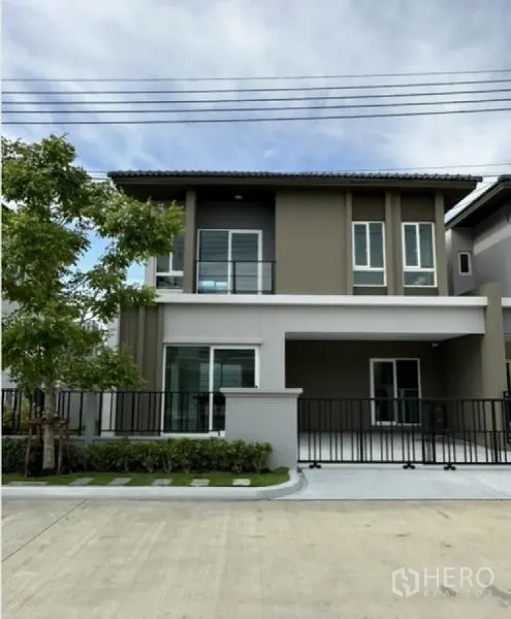 Townhouse for rent in Bang Phli, Samut Prakan - Front elevation of the townhouse with driveway, fence and greenery.