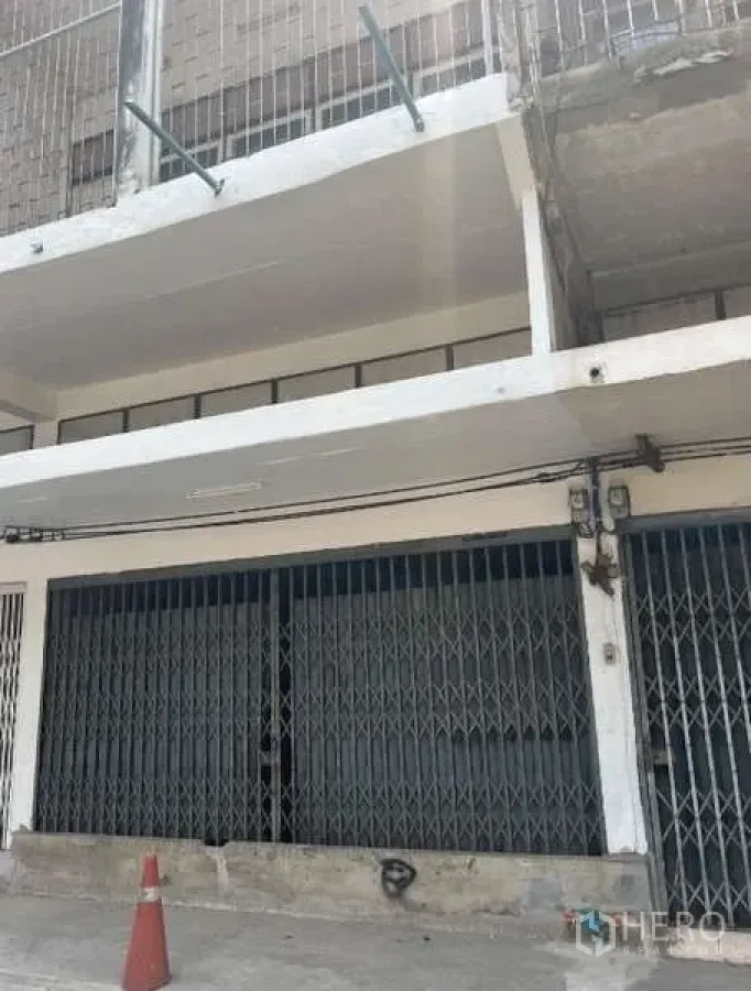 Shophouse for sale - Street-level view of a multi-storey shophouse with white concrete balconies and steel folding gates.