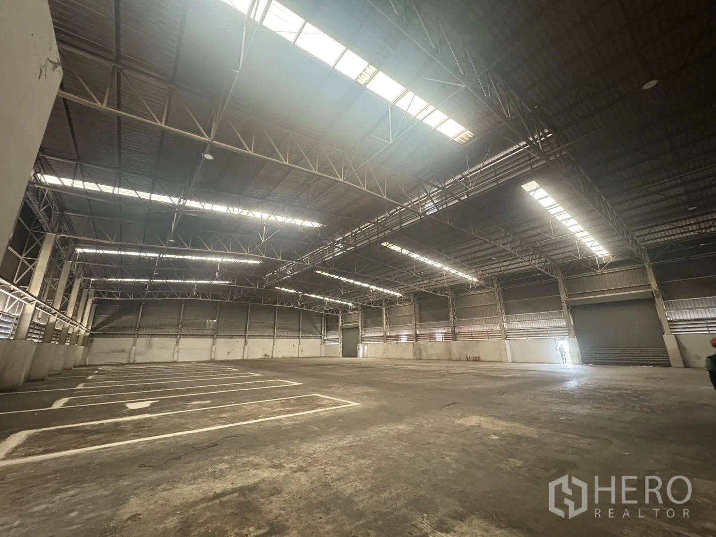 Factory for rent or sale in Samut Prakan - Wide industrial floor with painted bay lines and a roller shutter door.