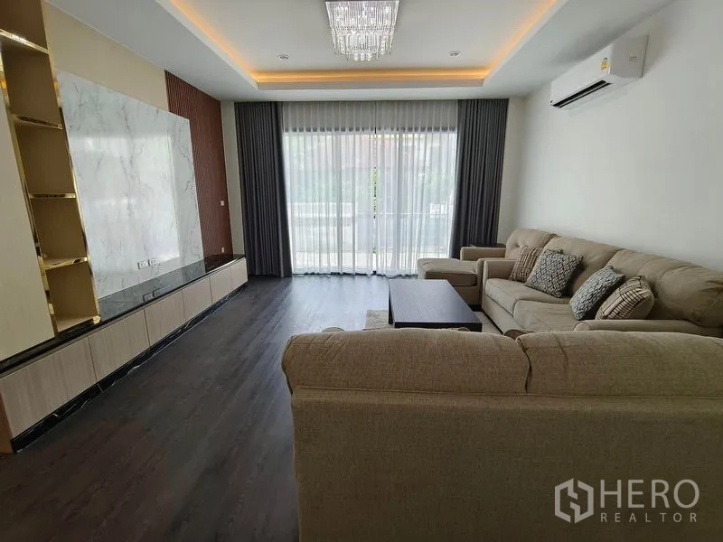 Detached House for rent or sale - Furnished lounge with sofa set, marble TV feature wall, chandelier, and sliding doors to a balcony.