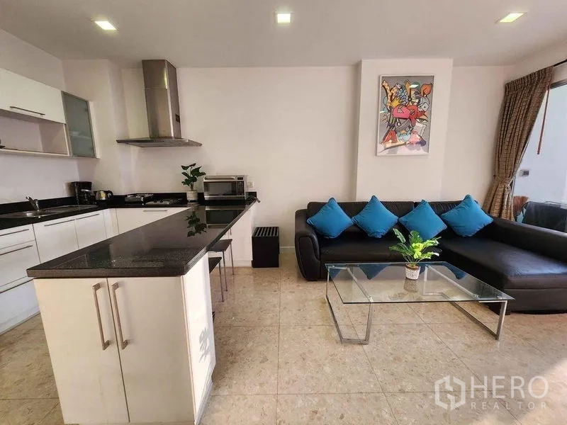 Condominium for rent in Khlong Toei, Bangkok - Living area with L-shaped sofa, glass coffee table and open kitchen layout.