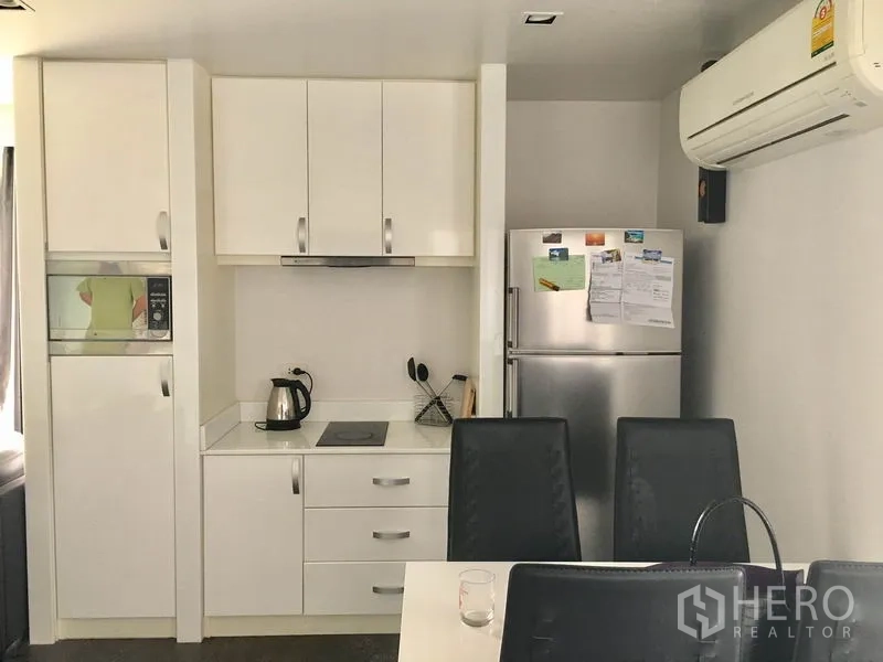 คอนโด ให้เช่าในWatthana, Bangkok - ครัวสีขาวบิลท์อินพร้อมตู้เก็บของ เตาไฟฟ้า ตู้เย็น และเก้าอี้รับประทานอาหาร